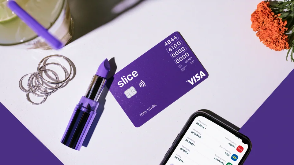 Purple Slice Visa card with a lipstick, rings and a phone on a desk